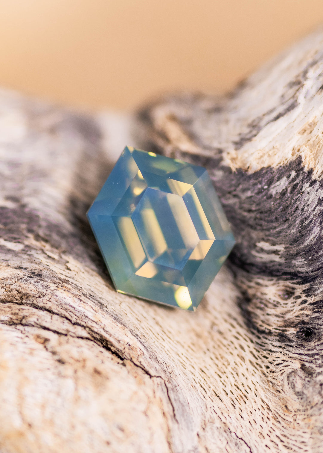 Opalescent teal sapphire faceted in a octagonal step cut resting on driftwood under natural light showing yellow reflections and vibrant teal coloring.