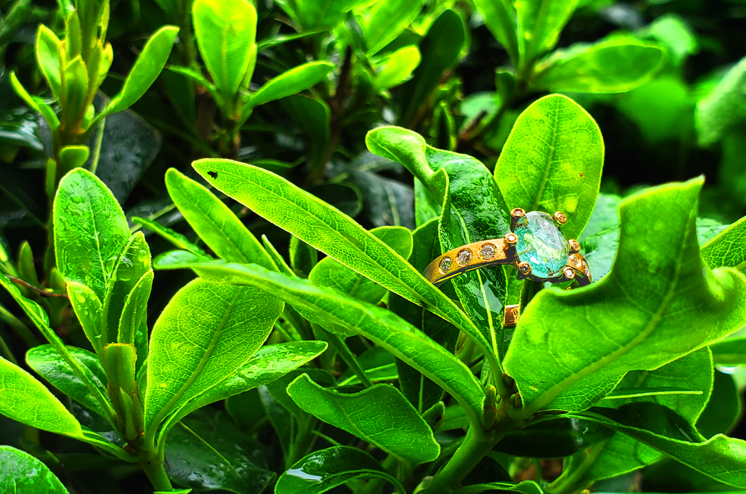 Unique custom green sapphire engagement ring resting in a vibrant green bush