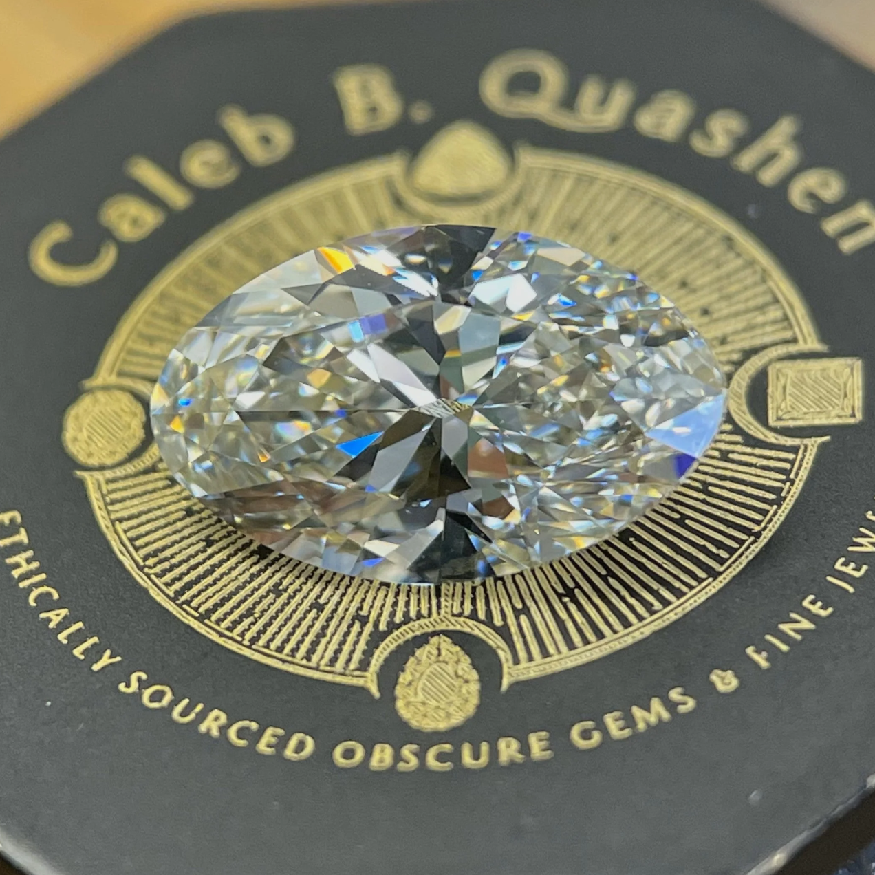 A stunning antique inspired elongated moval brilliant cut colorless diamond nestled atop a gem loupe, macro image showcasing the natural diamond with unique logo on the loupe in the background.