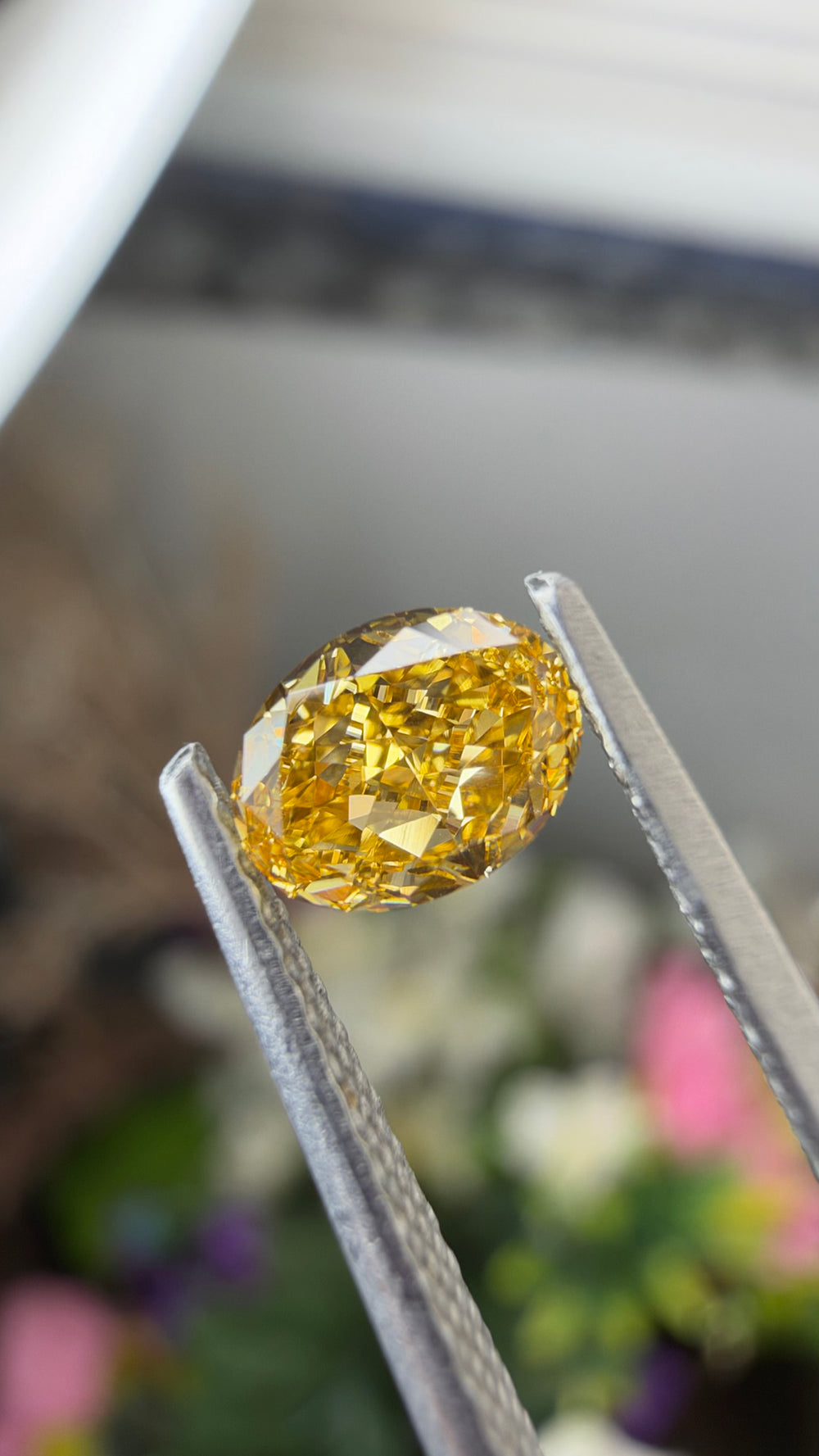 Detailed photograph of a 0.48ct Fancy Intense Yellow Orange diamond highlighting its oval-cut faceting, vivid color and 1.32 length-to-width ratio.
