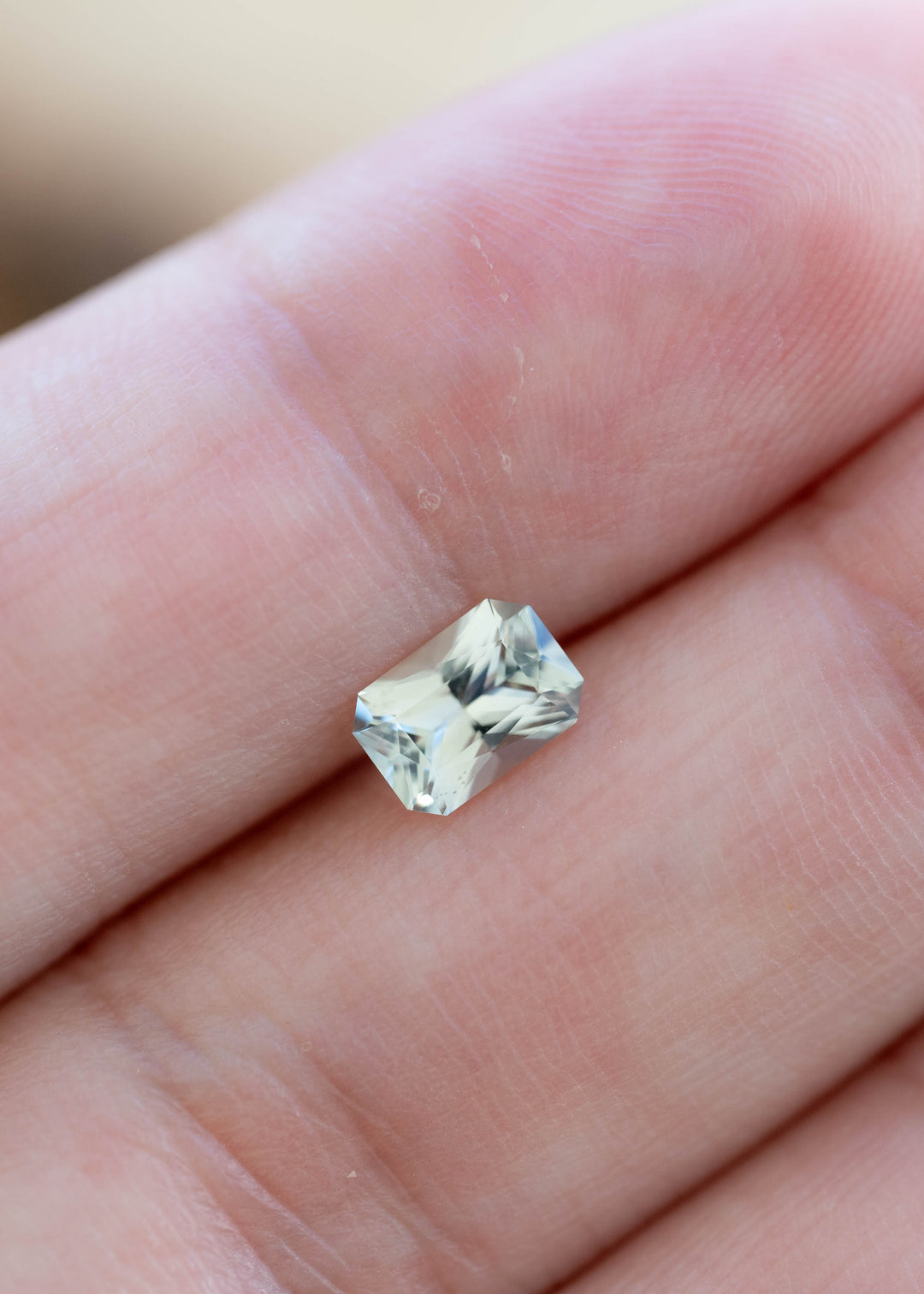 Natural seafoam green Montana sapphire weighing 0.695 carats shown on fingertips to illustrate its precision radiant cut and scale.