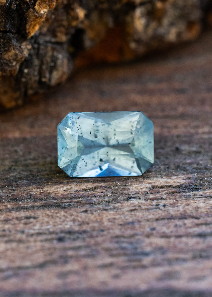 Natural 0.71 carat untreated Montana sapphire displaying smoky aqua blue color in a precision radiant cut with visible natural inclusions.