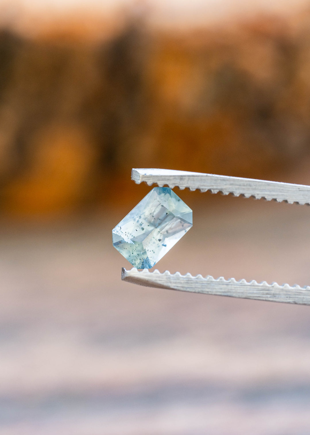 Close-up of an untreated Montana sapphire featuring a precision radiant cut, smoky aqua blue color, and distinctive natural crystal inclusions.