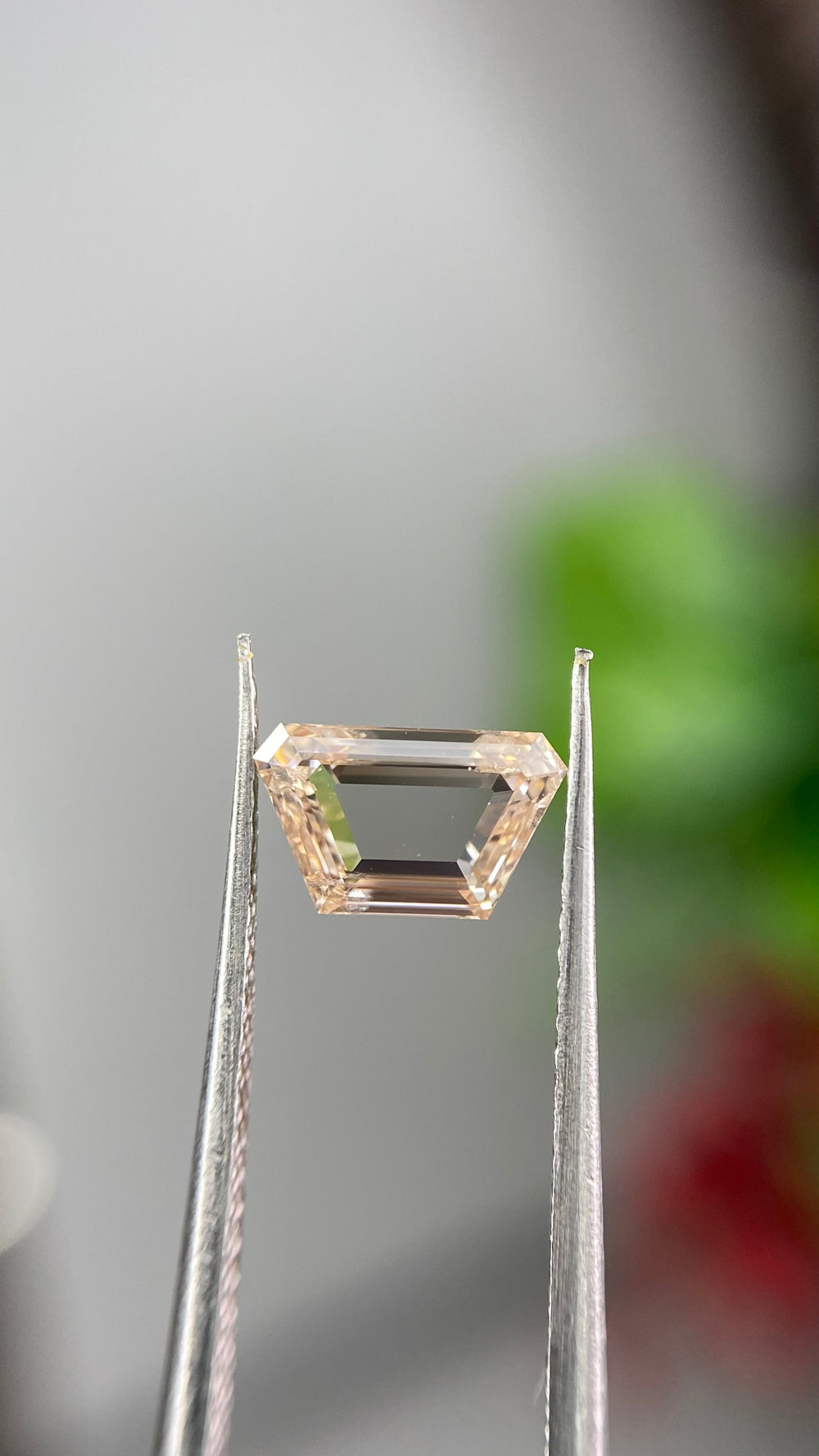Detailed photography of a 0.74ct Fancy Orangy Pink diamond highlighting its portrait-cut structure and distinctive fancy color.