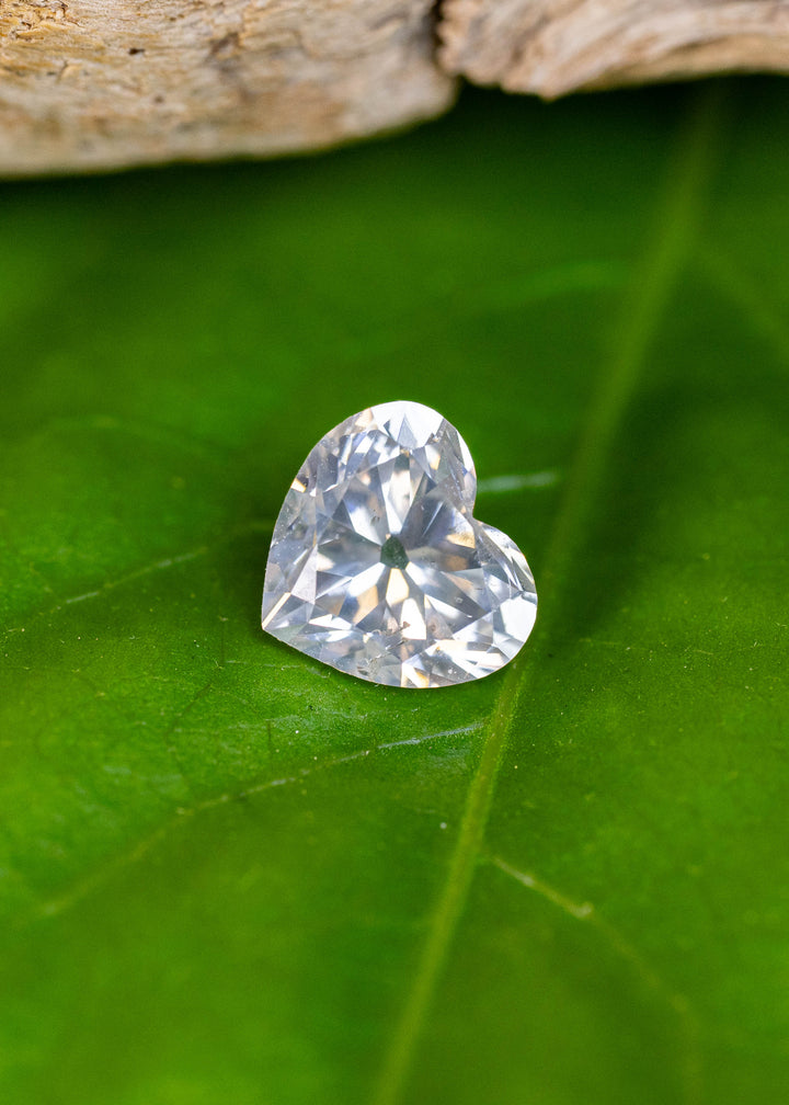 Natural 0.87 carat white diamond with an antique style heart cut displayed on a green leaf, showcasing exceptional brilliance and balanced symmetry.
