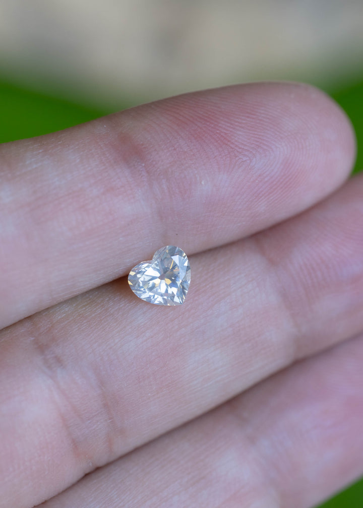 Natural 0.87 carat antique style heart cut white diamond displayed on a fingertip for scale, showing bright colorless brilliance.