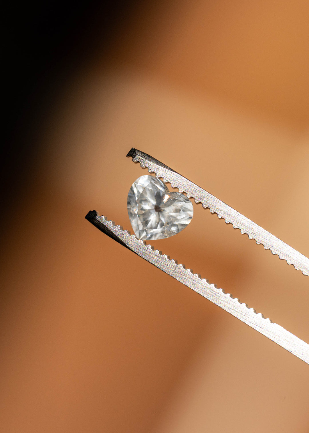 Close-up of a natural antique style heart cut white diamond held in tweezers, displaying crisp brilliance and precise faceting.