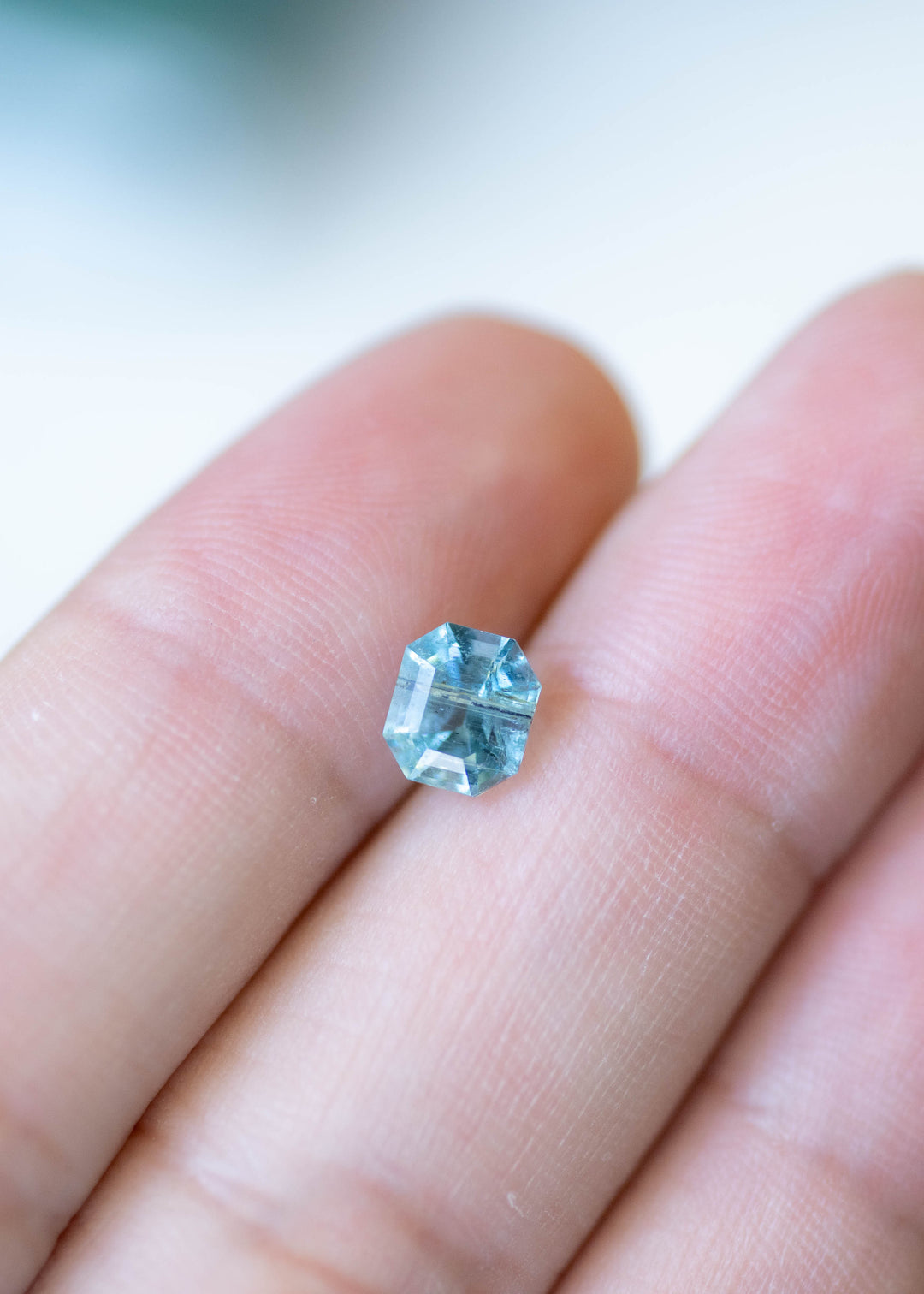 Natural deep teal aquamarine resting on fingertips, highlighting its custom octagonal step cut and face-up size.