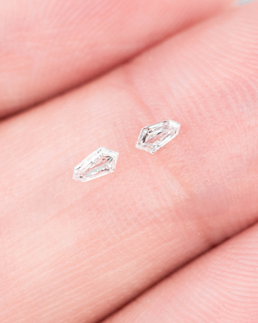 Two 0.10ct F-G color VVS clarity kite step cut diamonds from South Africa resting on fingertips, highlighting size, clarity, step faceting, and sparkle for jewelry design and melee diamond selection.
