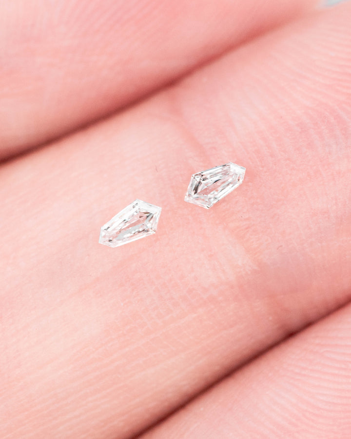 Two 0.10ct F-G color VVS clarity kite step cut diamonds from South Africa resting on fingertips, highlighting size, clarity, step faceting, and sparkle for jewelry design and melee diamond selection.