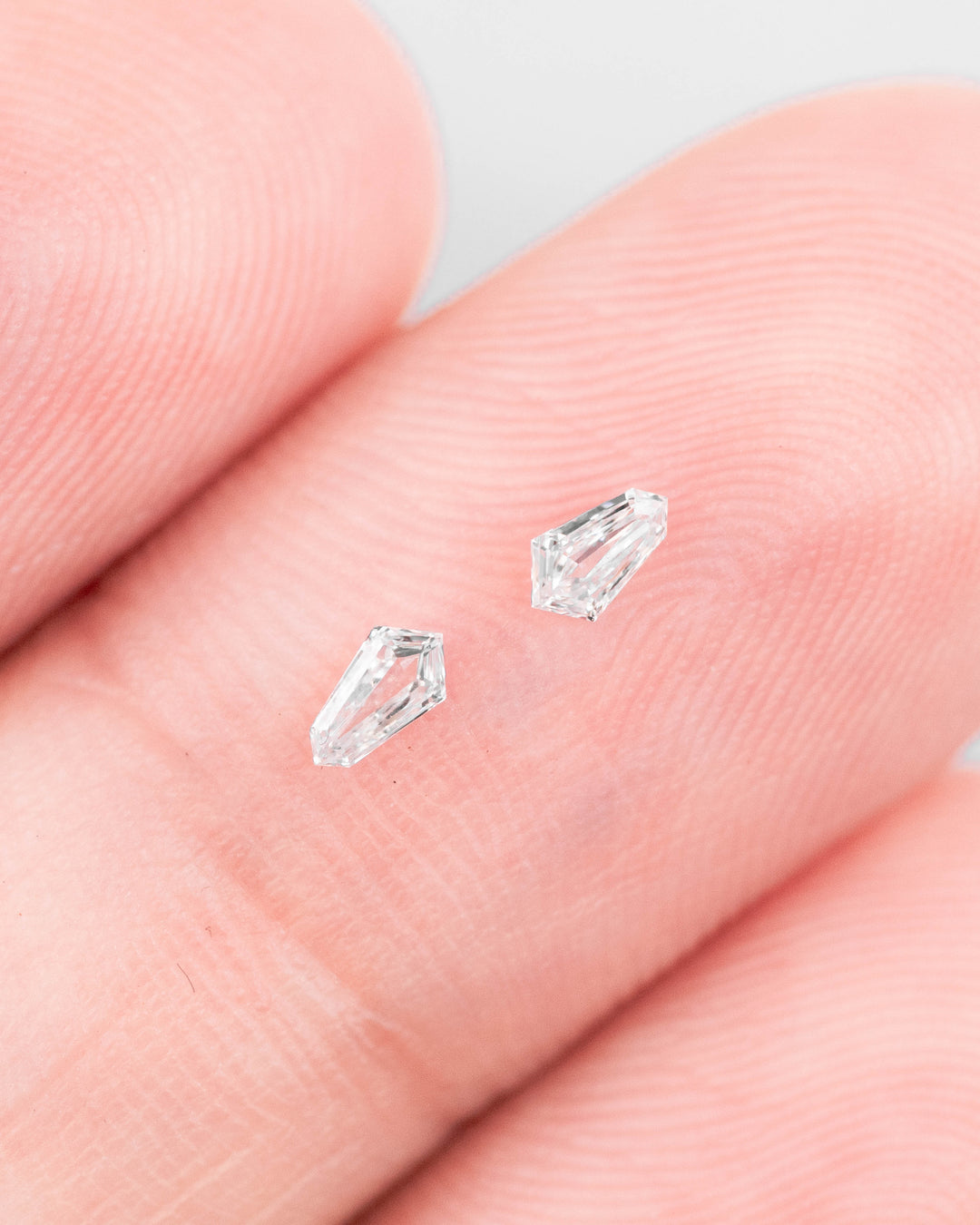 0.12-carat D-color VVS kite step cut diamonds displayed on a fingertip to show scale and clarity; precision matched diamond pair from South Africa with no treatment.