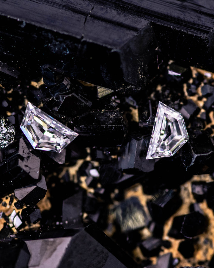 Macro image of a matching 0.18 carat D–E color VVS clarity Cadillac cut diamond pair from South Africa resting on dark tourmaline crystals. The stones exhibit crisp symmetry and natural brilliance.