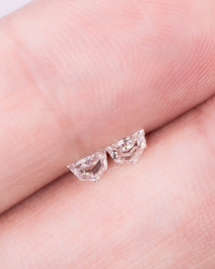 Close-up image of a 0.18 carat E–F color VVS clarity Cadillac cut diamond pair on a fingertip. The South African diamonds sparkle with sharp facets and reflect light with exceptional brilliance.