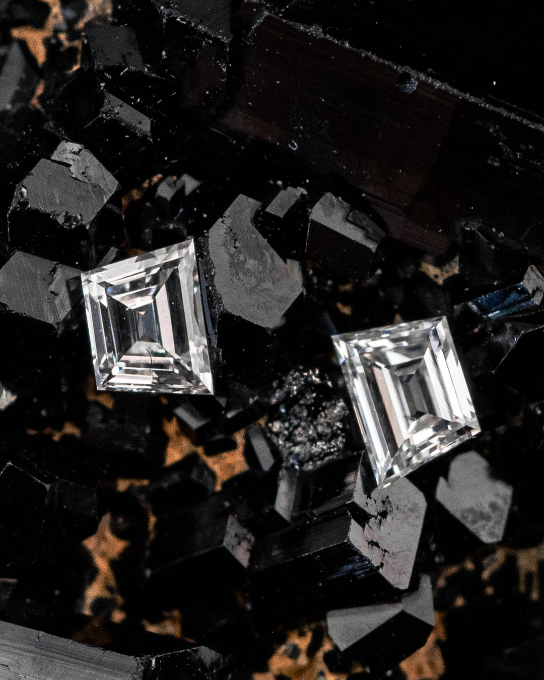 Pair of 0.18 carat F-G color VVS clarity Trapezoid step cut diamonds displayed on a black crystal mineral matrix, showcasing the geometric faceting, sparkle, and precision cutting of the matched diamond pair from South Africa.