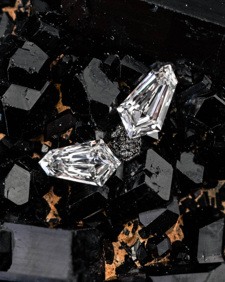 Two 0.18-carat D–E color VVS clarity kite step cut diamonds displayed on a black crystal mineral background, showing precision faceting and matched shapes, ethical diamonds from South Africa.