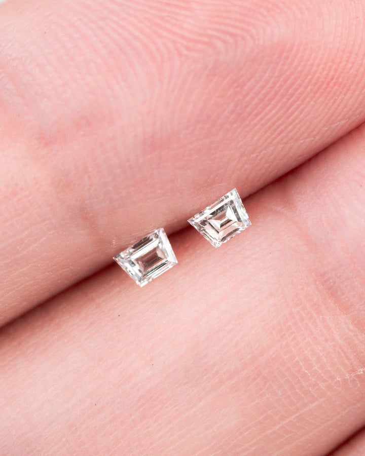 0.18 carat E color VVS clarity Trapezoid step cut diamond pair displayed on a fingertip, showing the matched geometric faceting and brilliance of the precision-cut South African diamonds.