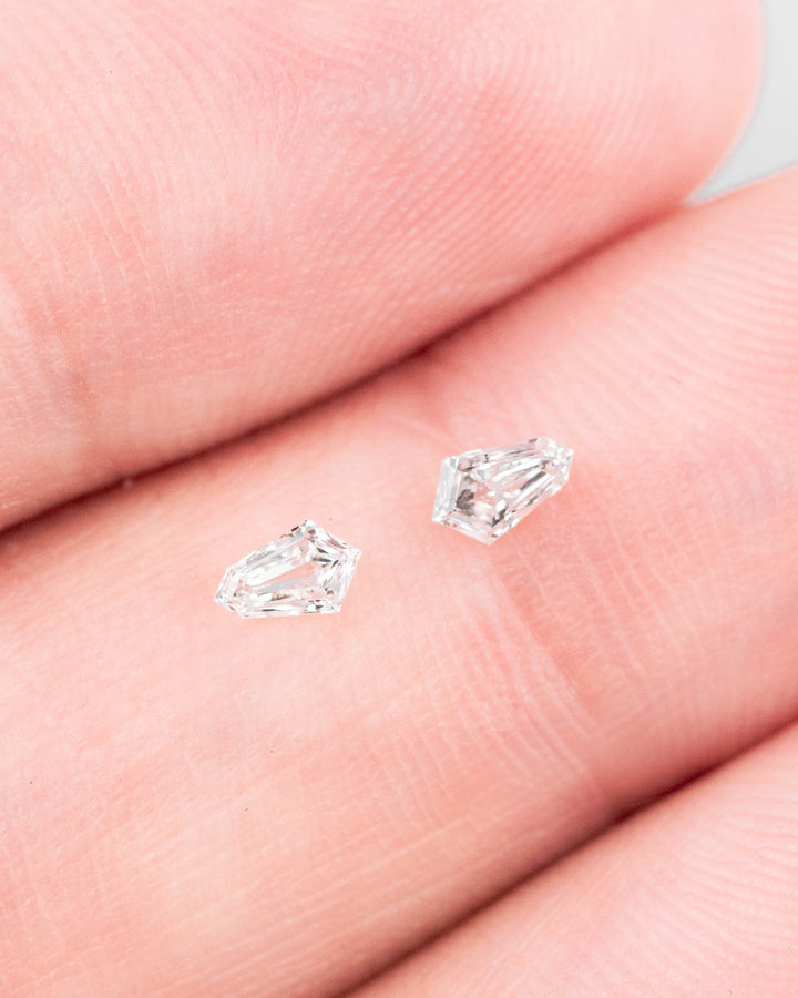 0.19 carat matched F-color kite step cut diamonds displayed on fingertips, showing clarity and precision faceting in natural light, ethical untreated South African diamond pair for fine jewelry.
