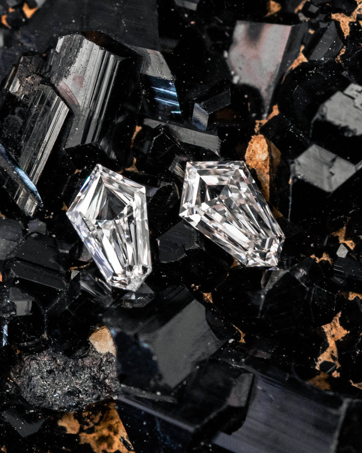 0.23 carat F–G color VVS clarity kite step cut diamond pair resting on a black crystal mineral matrix, highlighting the angular faceting, sparkle, and symmetry of the South African precision-cut diamonds.