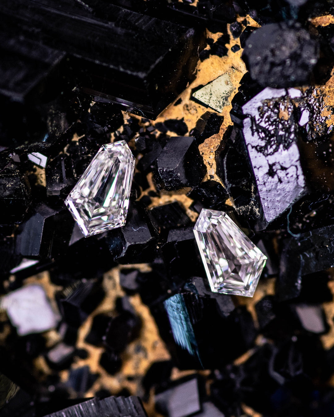 Close-up of two 0.28 carat G–H color VVS clarity Cadillac cut diamonds from South Africa resting on a dark mineral background. The matching pair highlights precision faceting, geometric brilliance, and ethical sourcing.