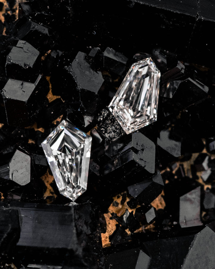 Matched pair of 0.28 carat E-F color VVS clarity kite step cut diamonds displayed on a black crystal mineral matrix, highlighting the sharp step-cut facets, symmetry, and natural brilliance of the stones.
