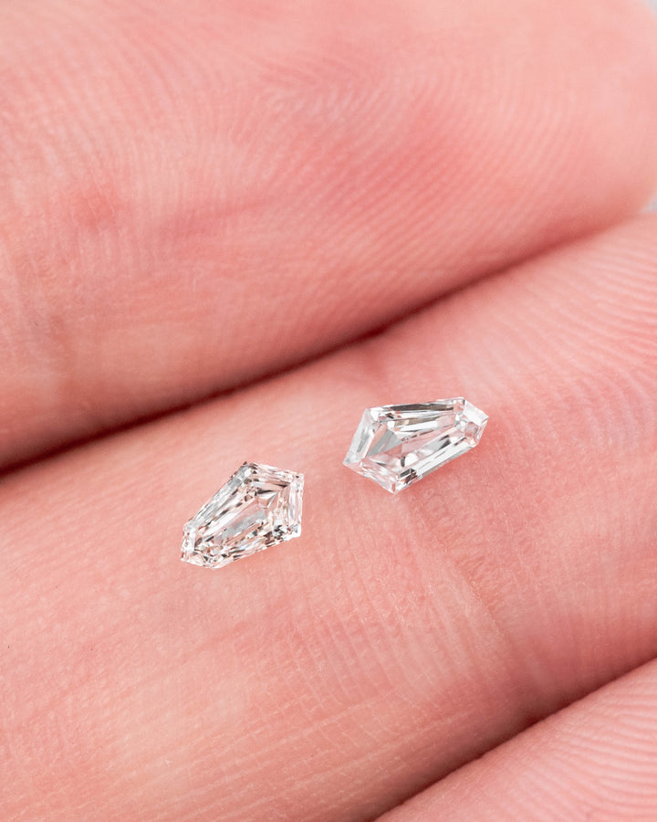 Pair of 0.28 carat E-F color VVS clarity kite step cut diamonds resting on a fingertip, showcasing their geometric faceting, brilliance, and precision matching for custom fine jewelry.