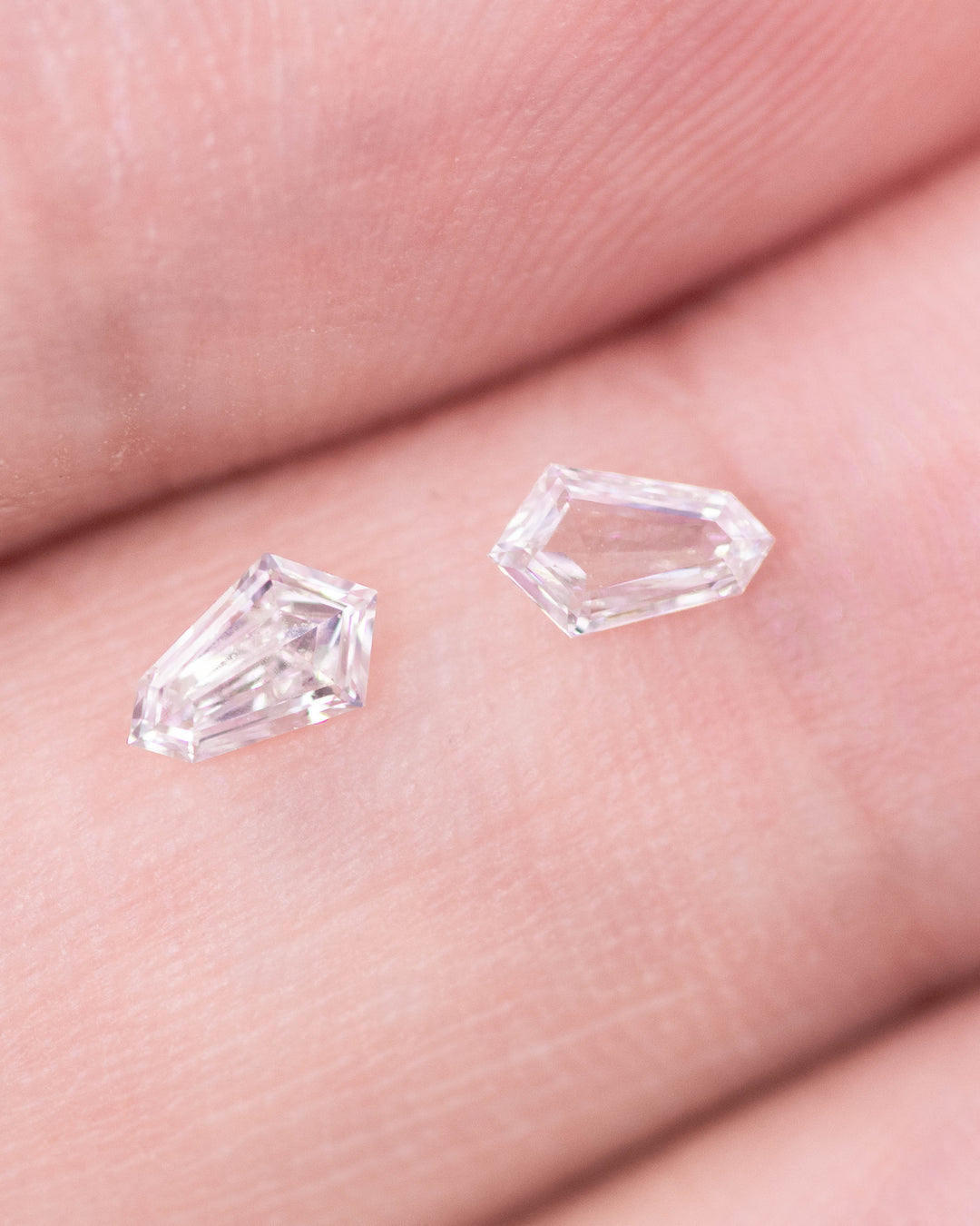 Close-up image of a 0.29 carat F–G color VVS–VS clarity Cadillac cut diamond pair from South Africa displayed on fingertips. The natural untreated diamonds show crisp step facets, symmetry, and brilliant sparkle.