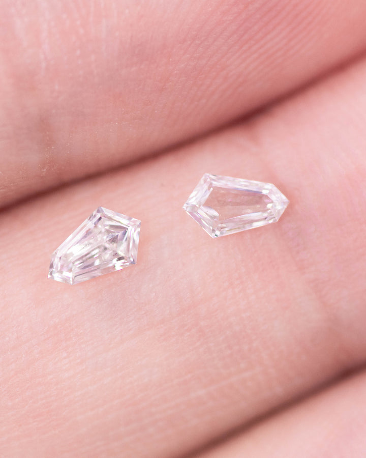 Close-up image of a 0.29 carat F–G color VVS–VS clarity Cadillac cut diamond pair from South Africa displayed on fingertips. The natural untreated diamonds show crisp step facets, symmetry, and brilliant sparkle.