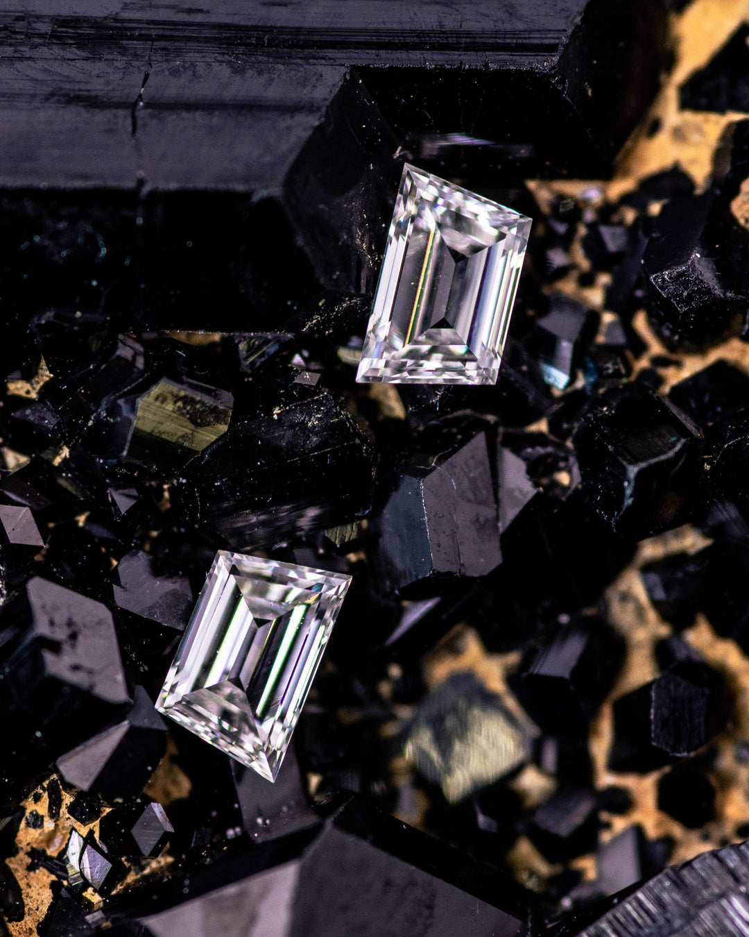 Macro photo of 0.30 carat G color VVS clarity trapezoid step cut diamond pair from South Africa resting on a bed of black tourmaline crystals. The untreated diamonds display geometric symmetry and sharp reflective brilliance.