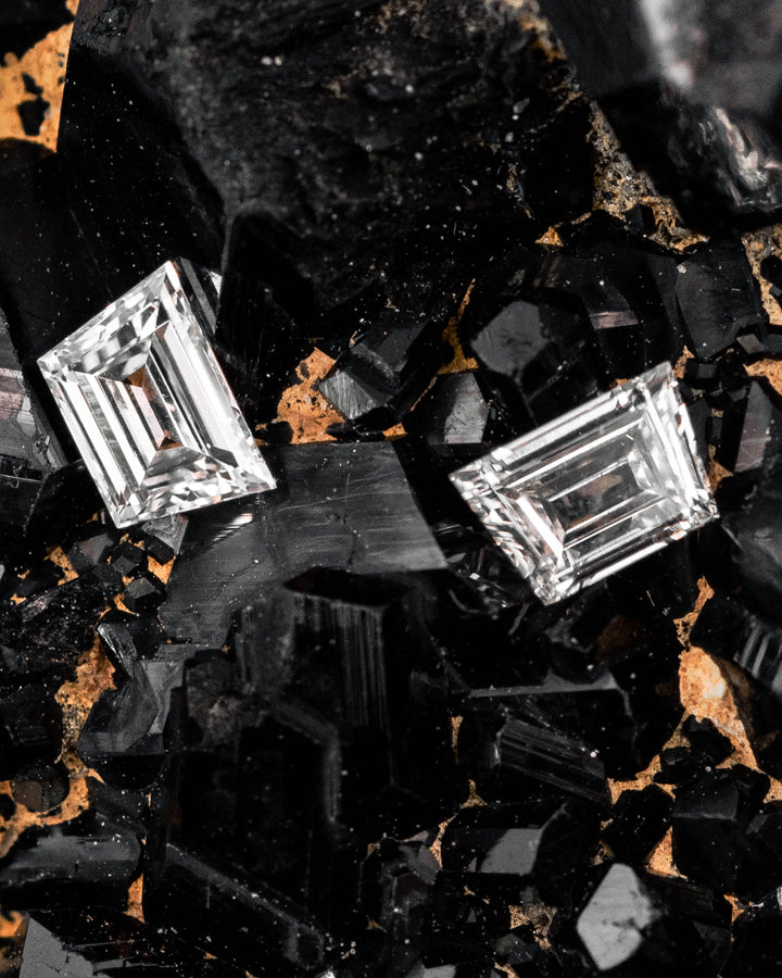 0.30 carat F-G color VVS clarity Trapezoid step cut diamonds from South Africa resting on a black crystal mineral matrix, highlighting the precision step-cut faceting and natural sparkle of the untreated matched pair.