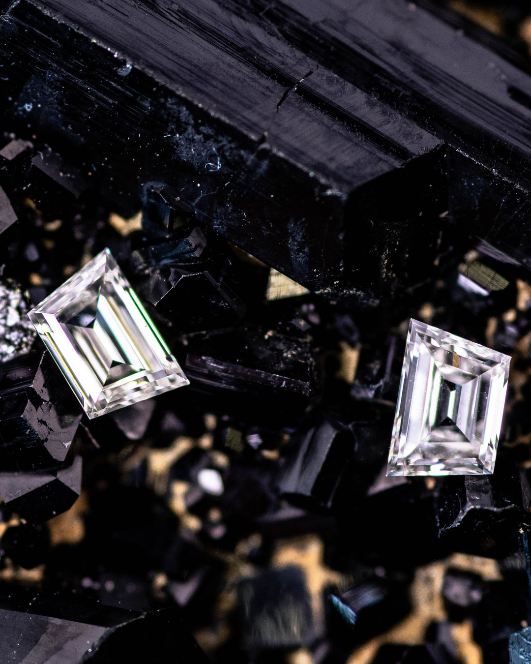 Macro photo of a 0.31 carat G–H color VVS clarity trapezoid step cut diamond pair from South Africa resting on black crystal matrix. The natural untreated diamonds display perfect symmetry, crisp step facets, and exceptional light reflection.