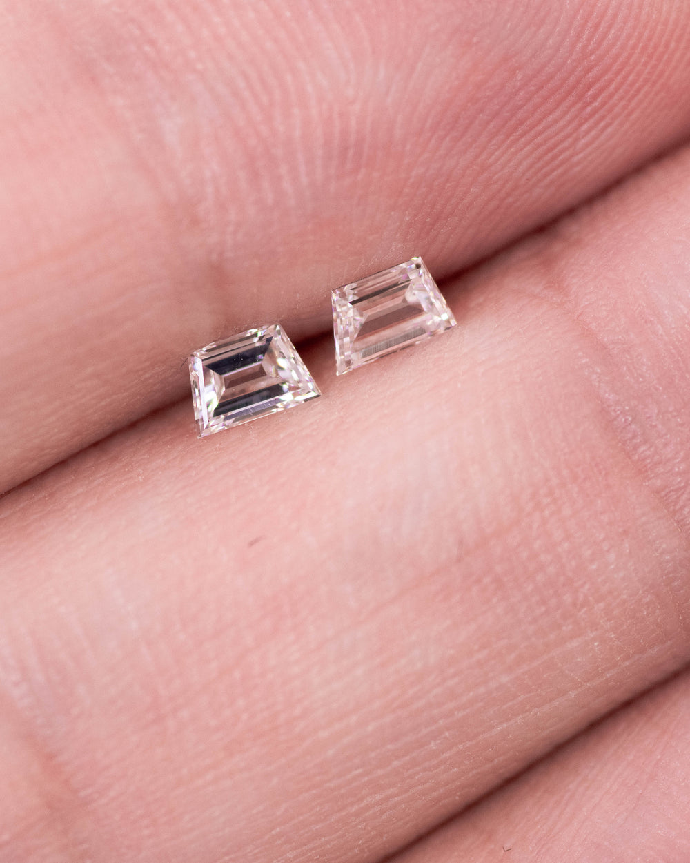 Close-up of a 0.31 carat E–F color VVS clarity trapezoid step cut diamond pair from South Africa resting on fingertips. The natural untreated diamonds display clean step facets, sharp symmetry, and bright white brilliance.