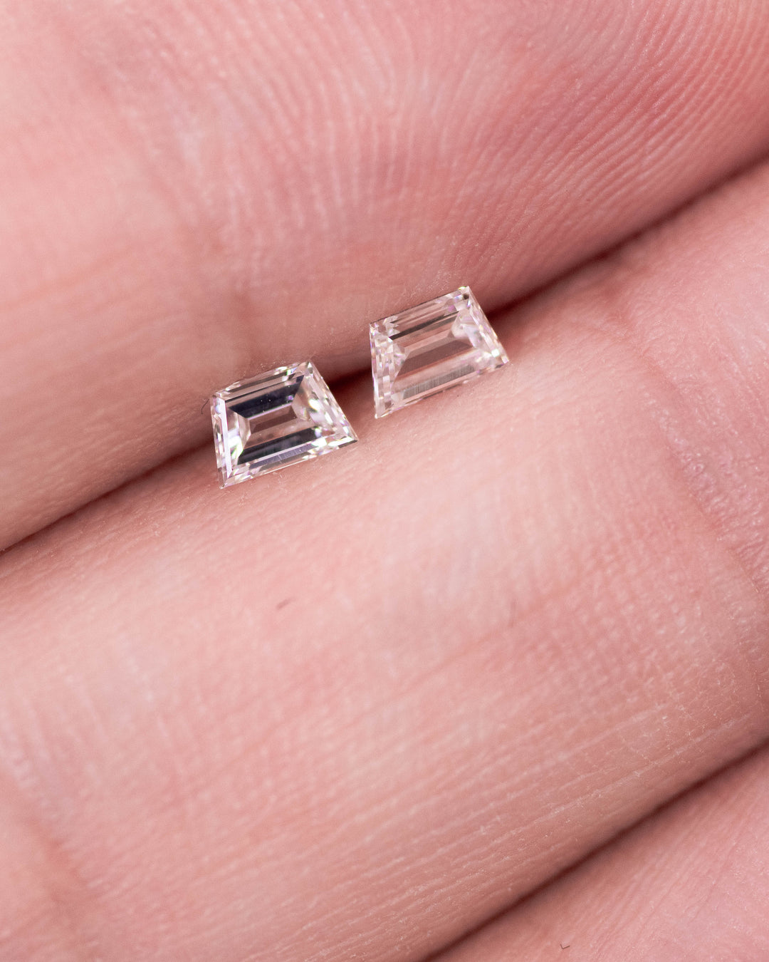 Close-up of a 0.31 carat E–F color VVS clarity trapezoid step cut diamond pair from South Africa resting on fingertips. The natural untreated diamonds display clean step facets, sharp symmetry, and bright white brilliance.