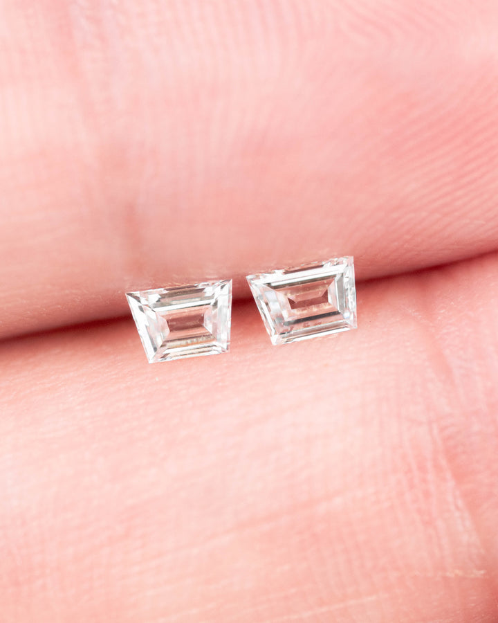 Matched pair of 0.32 carat F color VVS clarity trapezoid step cut diamonds from South Africa displayed on fingertips, showcasing their symmetrical faceting, brilliance, and untreated natural diamond quality.