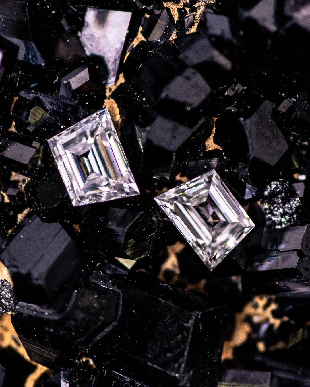 Macro photo of 0.33 carat E–F color VS clarity trapezoid step cut diamond pair from South Africa placed on black tourmaline crystal matrix. The untreated diamonds show precision faceting, geometric balance, and bright reflective fire.
