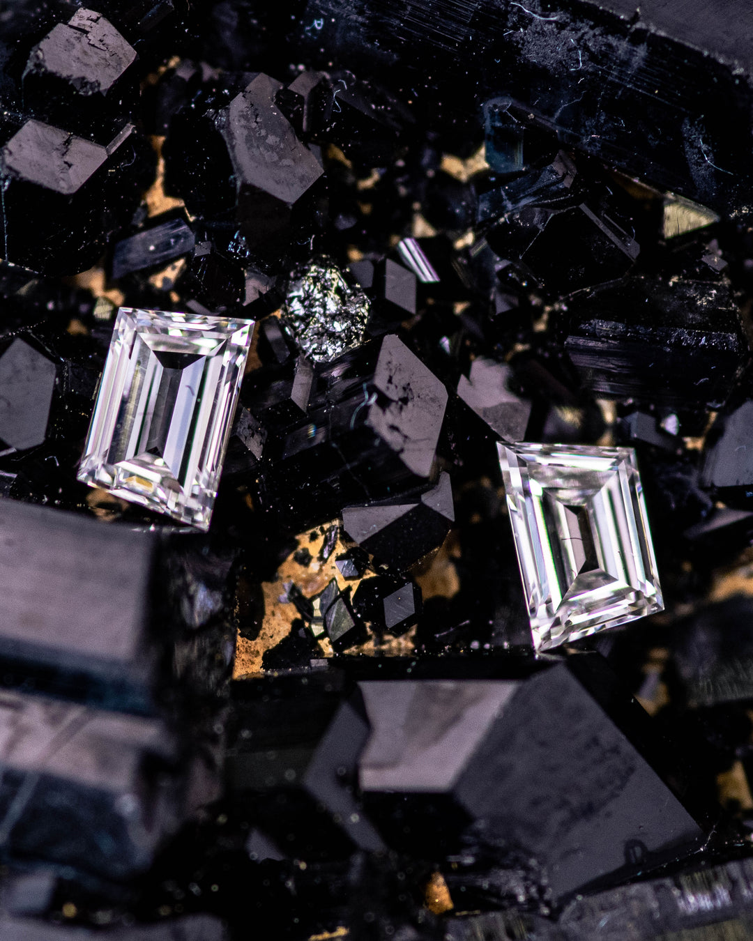 Macro photo of 0.33 carat F color VVS clarity trapezoid step cut diamond pair from South Africa resting on a natural black crystal matrix. The untreated diamonds feature crisp step facets, symmetrical geometry, and high brilliance under close-up lighting.