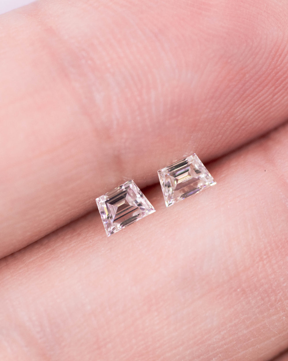 Close-up of a 0.33 carat E–F color VS clarity trapezoid step cut diamond pair from South Africa resting on fingertips. The natural untreated diamonds display crisp mirror-like step facets, matched symmetry, and clean light performance.