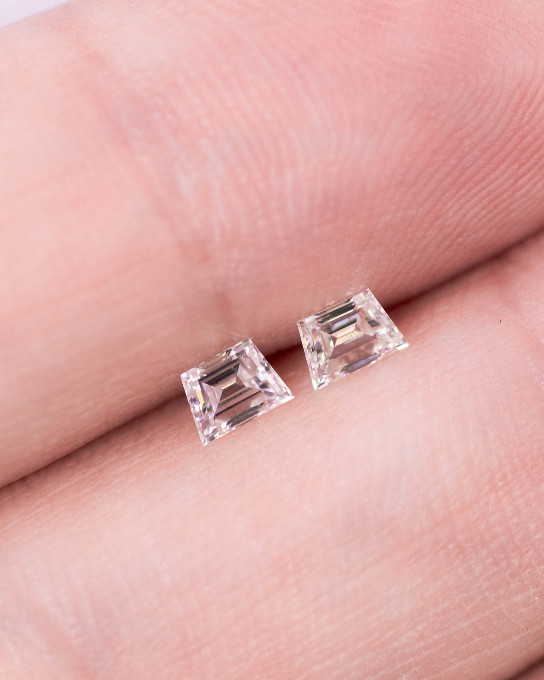 Close-up of a 0.33 carat E–F color VS clarity trapezoid step cut diamond pair from South Africa resting on fingertips. The natural untreated diamonds display crisp mirror-like step facets, matched symmetry, and clean light performance.
