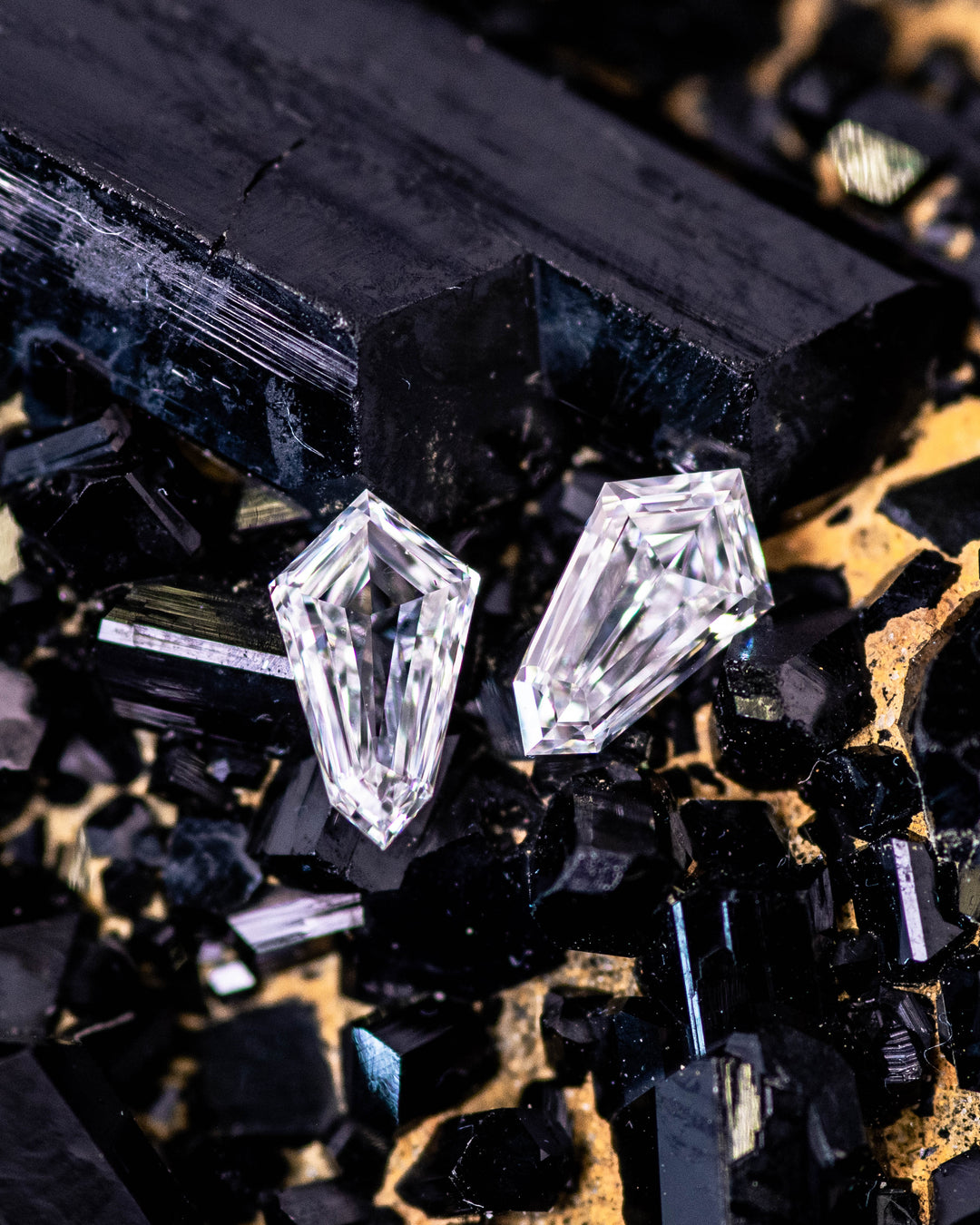 Macro photo of two 0.34 carat D color VVS clarity kite step cut diamonds from South Africa resting on dark crystal matrix. The natural untreated stones highlight angular symmetry, clarity, and reflective sparkle.