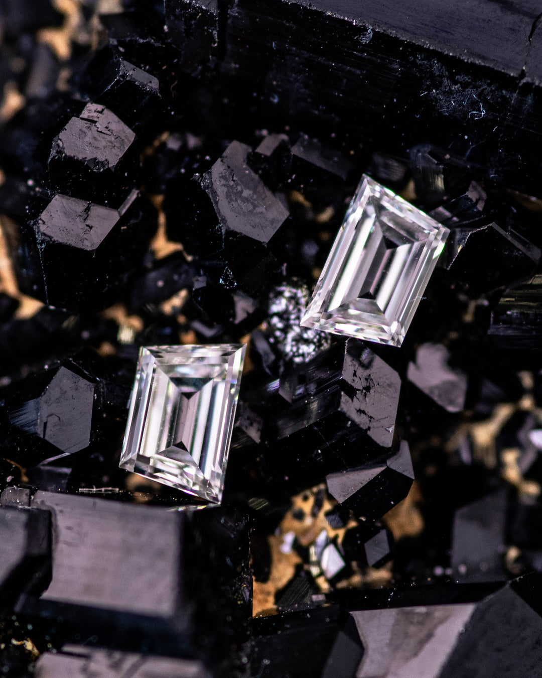 Macro image of 0.34 carat G color VVS clarity trapezoid step cut diamond pair from South Africa resting on a black mineral crystal surface. The untreated diamonds show sharp step facets, geometric brilliance, and exceptional clarity.