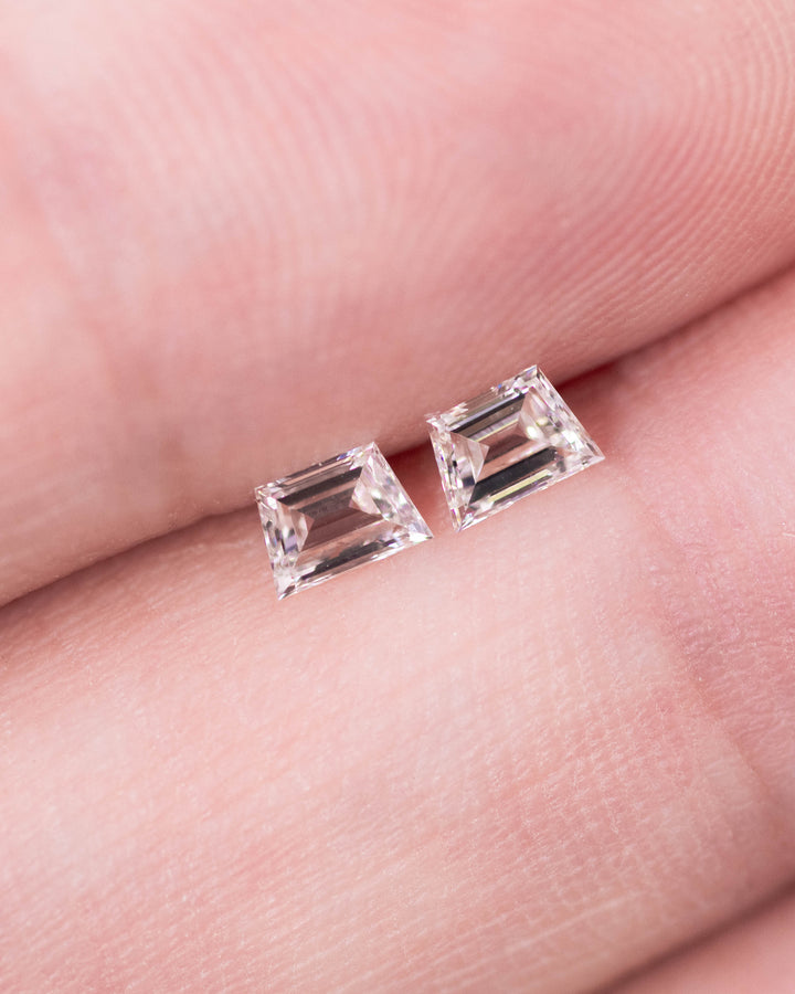 Close-up of a 0.34 carat F–G color VVS clarity trapezoid step cut diamond pair from South Africa displayed on fingertips. The natural untreated diamonds show clean geometry, excellent matching proportions, and high brilliance under natural light.