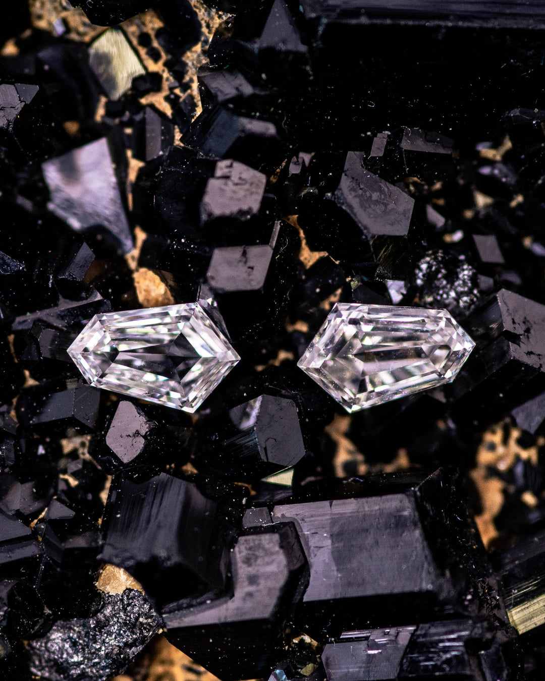Macro photo of two 0.35 carat D color VVS clarity kite step cut diamonds from South Africa resting on dark mineral crystals. The natural untreated stones reveal clean lines, clarity, and exceptional craftsmanship.
