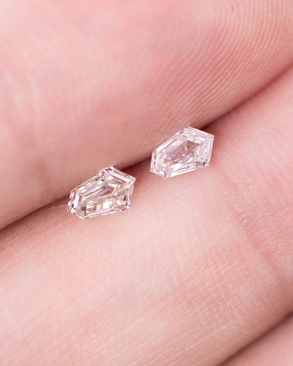 Close-up of a 0.35 carat D color VVS clarity kite step cut diamond pair from South Africa shown on fingertips. The natural untreated diamonds display precision step facets and sharp kite geometry with mirror-like brilliance.