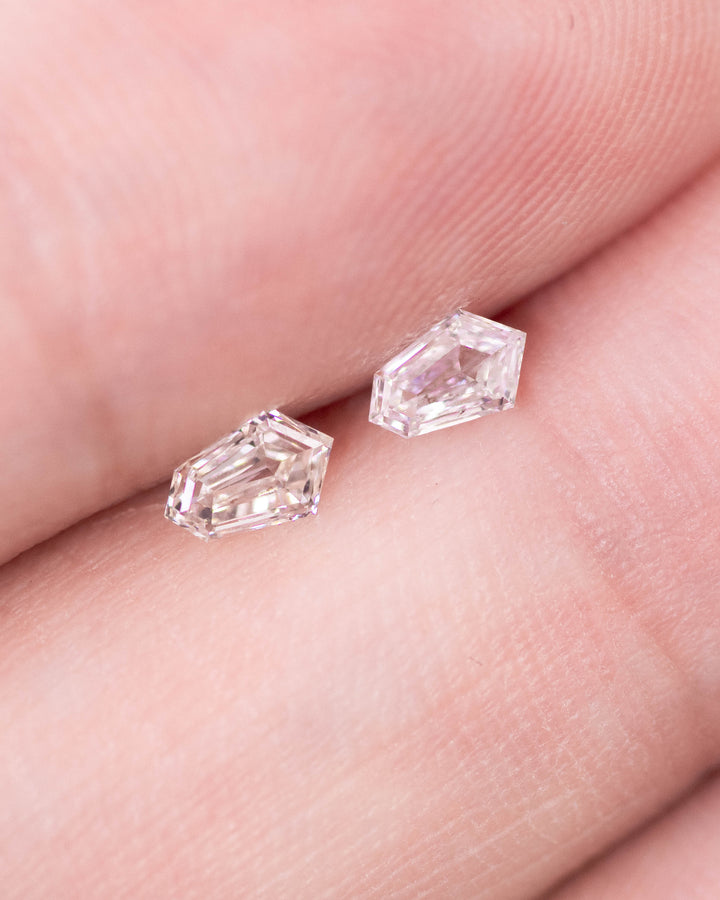 Close-up of a 0.35 carat D color VVS clarity kite step cut diamond pair from South Africa shown on fingertips. The natural untreated diamonds display precision step facets and sharp kite geometry with mirror-like brilliance.