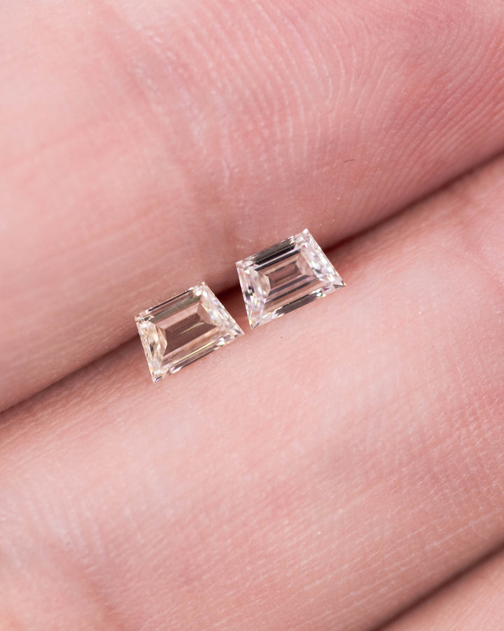 Close-up of 0.38 carat G–H color VVS clarity trapezoid step cut diamond pair from South Africa displayed on fingertips. The natural untreated diamonds reveal precision faceting, excellent matching proportions, and bright reflective sparkle.