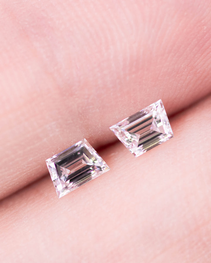 Close-up of a 0.42 carat D color VVS clarity trapezoid step cut diamond pair from South Africa displayed on fingertips. The natural untreated diamonds show excellent symmetry, high polish, and bright white fire ideal for fine jewelry settings.