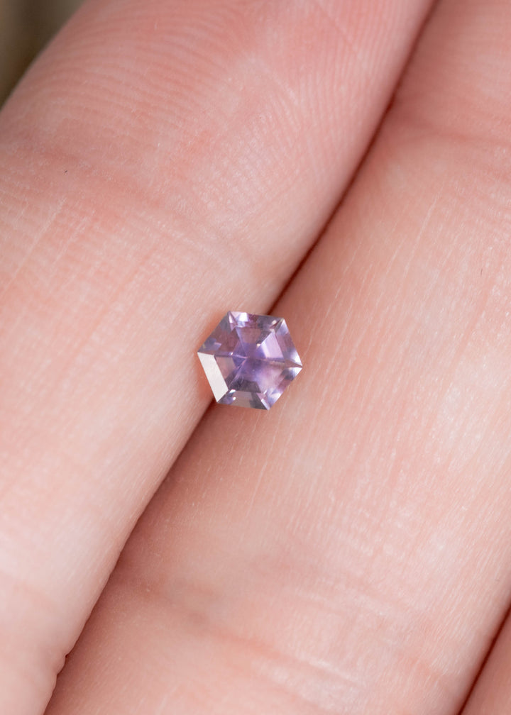 0.42 carat lavender purple pink Montana sapphire resting on finger, precision hexagon step cut gemstone from El Dorado Bar Deposit highlighting compact size and geometric custom jewelry appeal