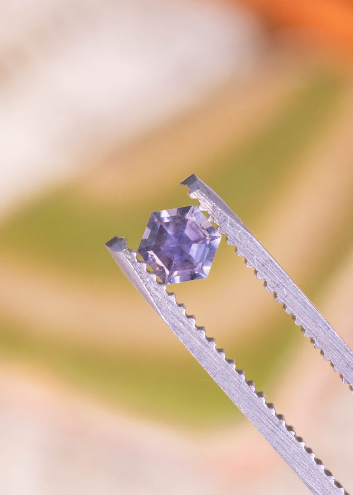 0.42 carat purple pink Montana sapphire hexagon step cut held in tweezers, untreated gemstone from El Dorado Bar Montana USA displaying sharp facet junctions, clean symmetry and reflective step cut brilliance