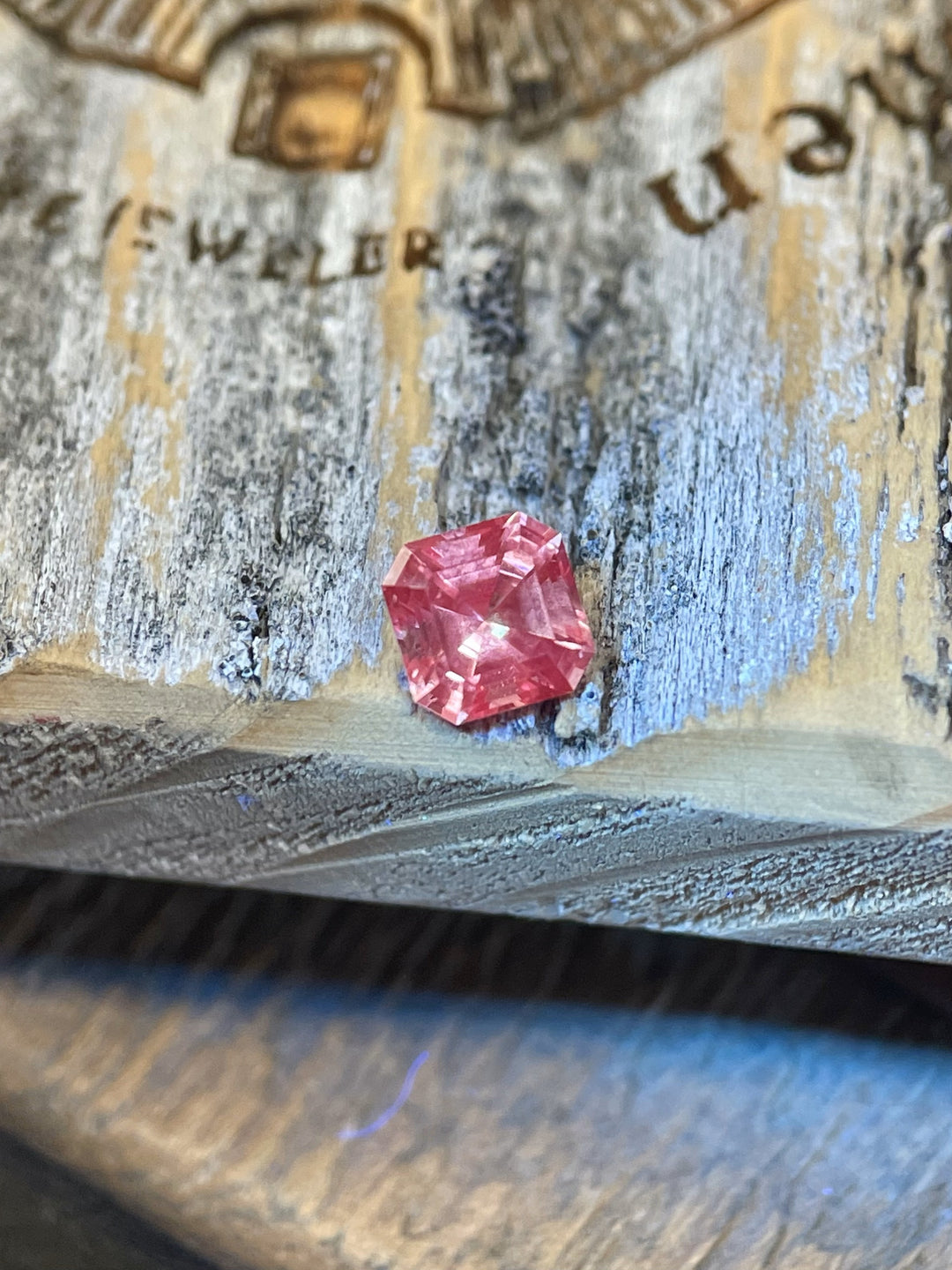 Close-up of a 0.56-carat Montana sapphire with a unique color shift from peach pink to vibrant strawberry pink, placed on a rustic wooden surface.