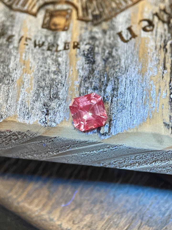 Close-up of a 0.56-carat Montana sapphire with a unique color shift from peach pink to vibrant strawberry pink, placed on a rustic wooden surface.