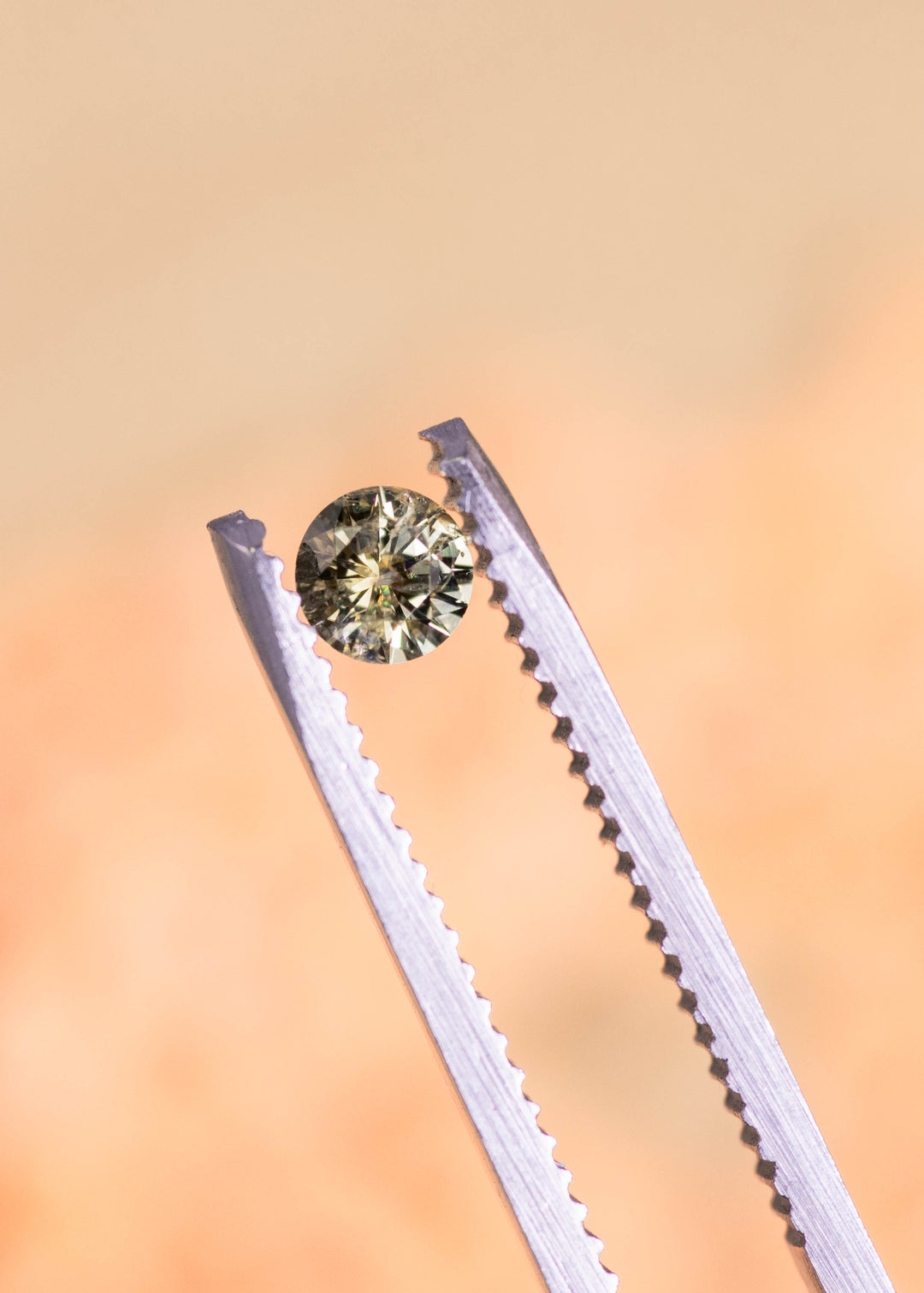 Loose yellow, teal and green Montana sapphire pair held in tweezers, highlighting the round brilliant cut and lively natural color under soft light.